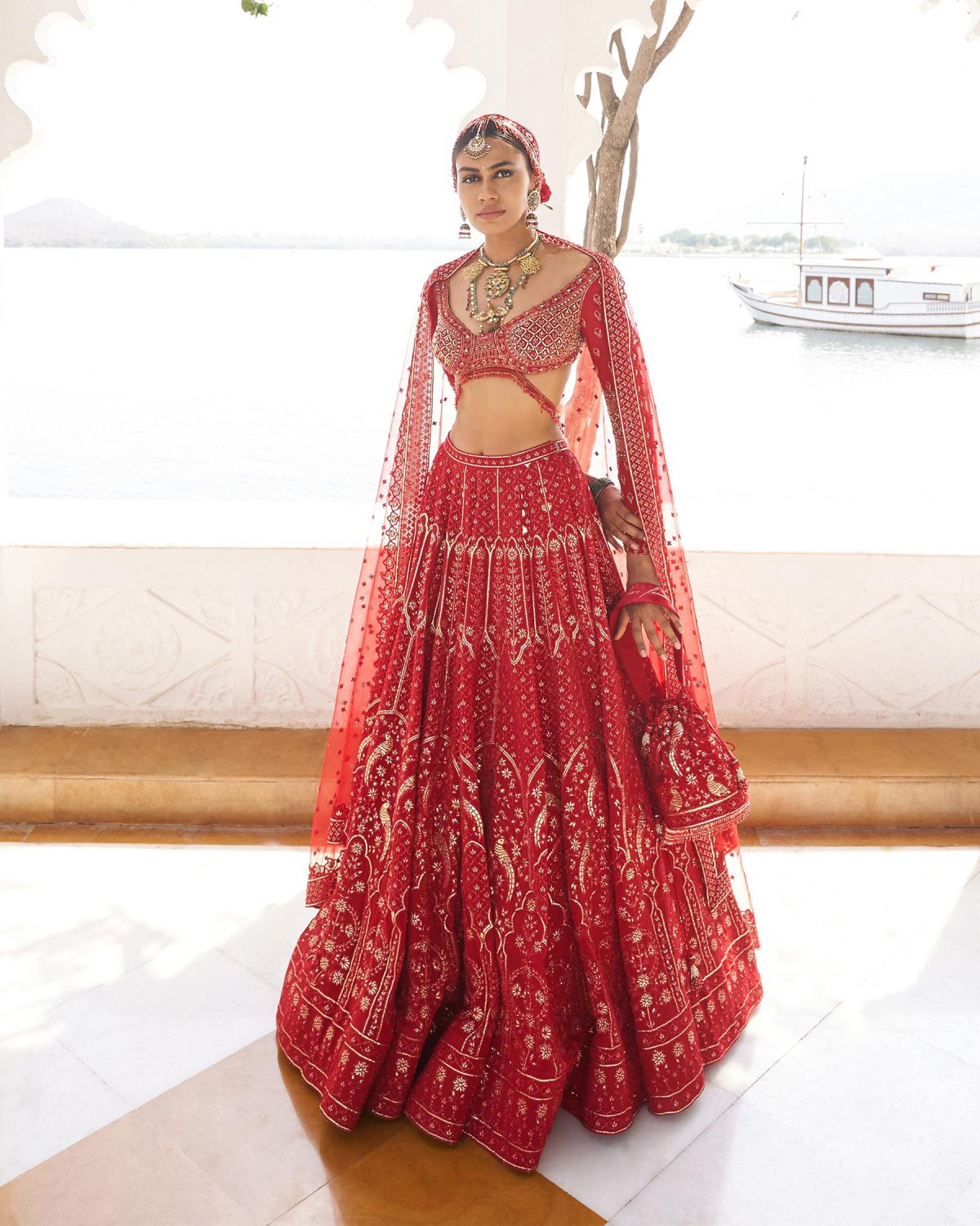 The red bridal Lehenga is coupled with a tulle Dupatta adorned with a border and Butti motifs